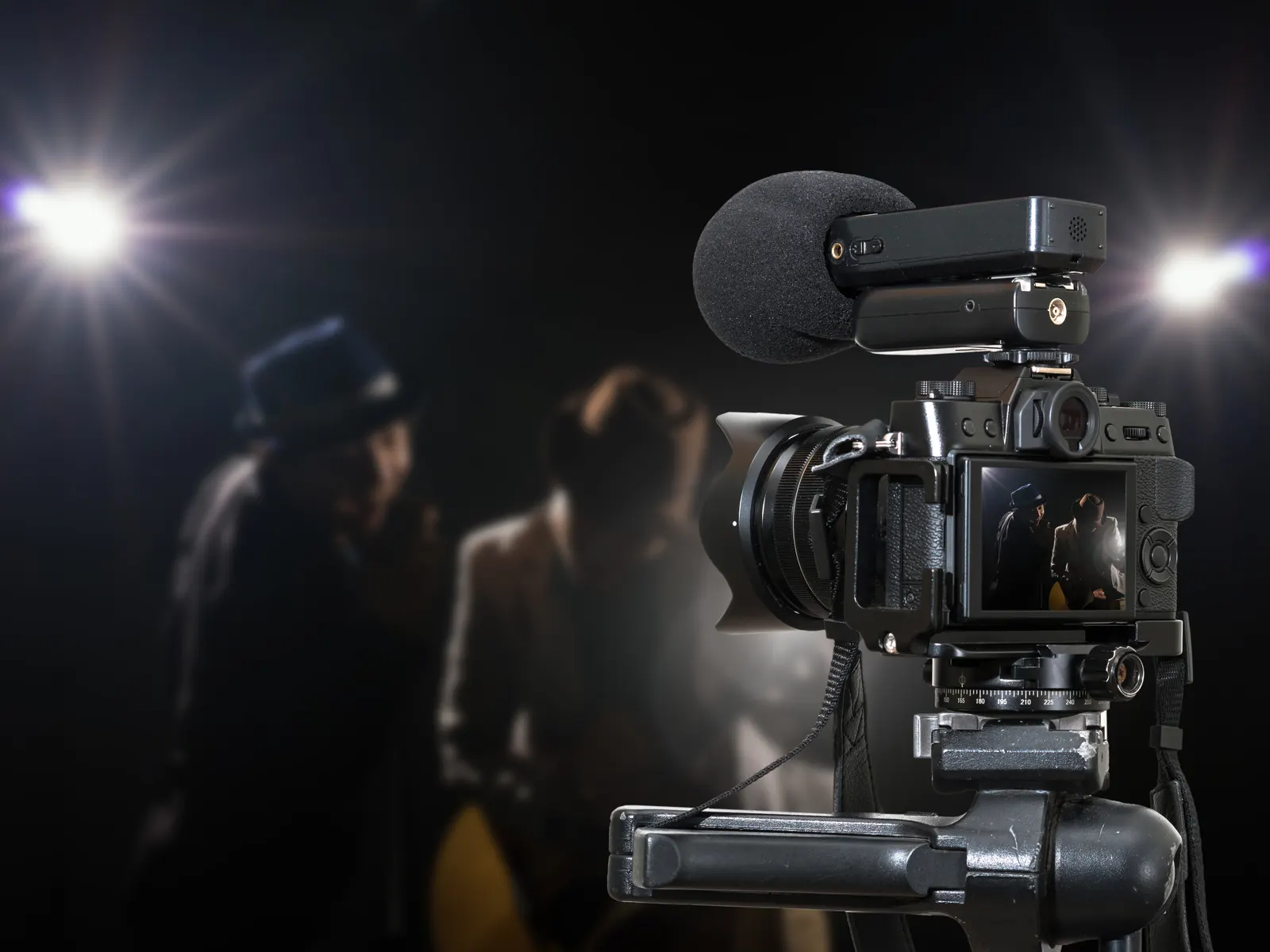Cinepresa su un set cinematografico con due figure sotto le luci